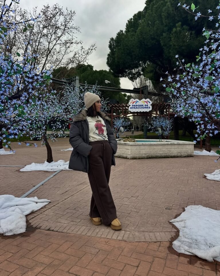 Laura Toledo posando en un parque con luces navideñas, usando abrigo y pantalones cómodos.