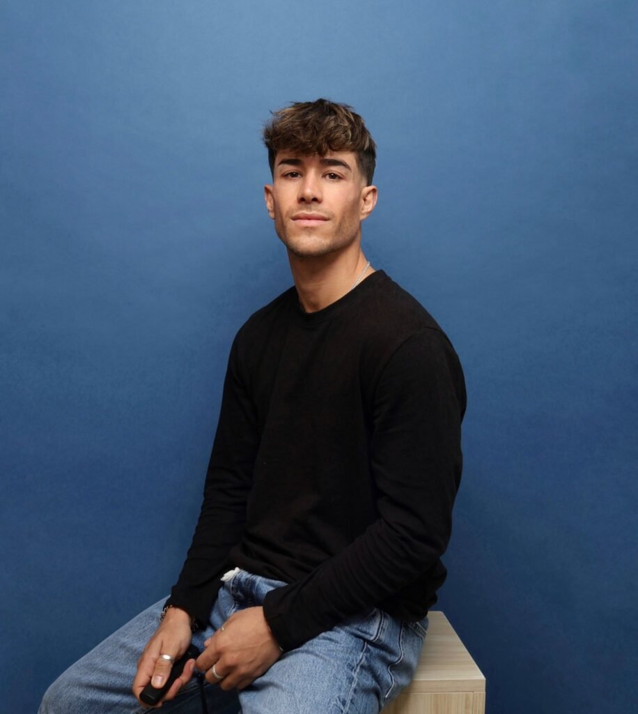 Uri Terradas posando con camiseta negra y jeans frente a un fondo azul.