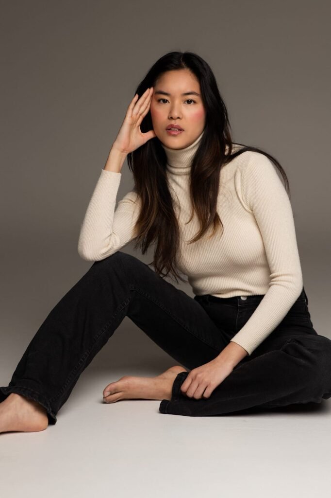 Retrato de Alba García sentada en un fondo neutro, con un suéter blanco y jeans negros. La imagen refleja su estilo sencillo pero elegante, con una expresión relajada y profesional.