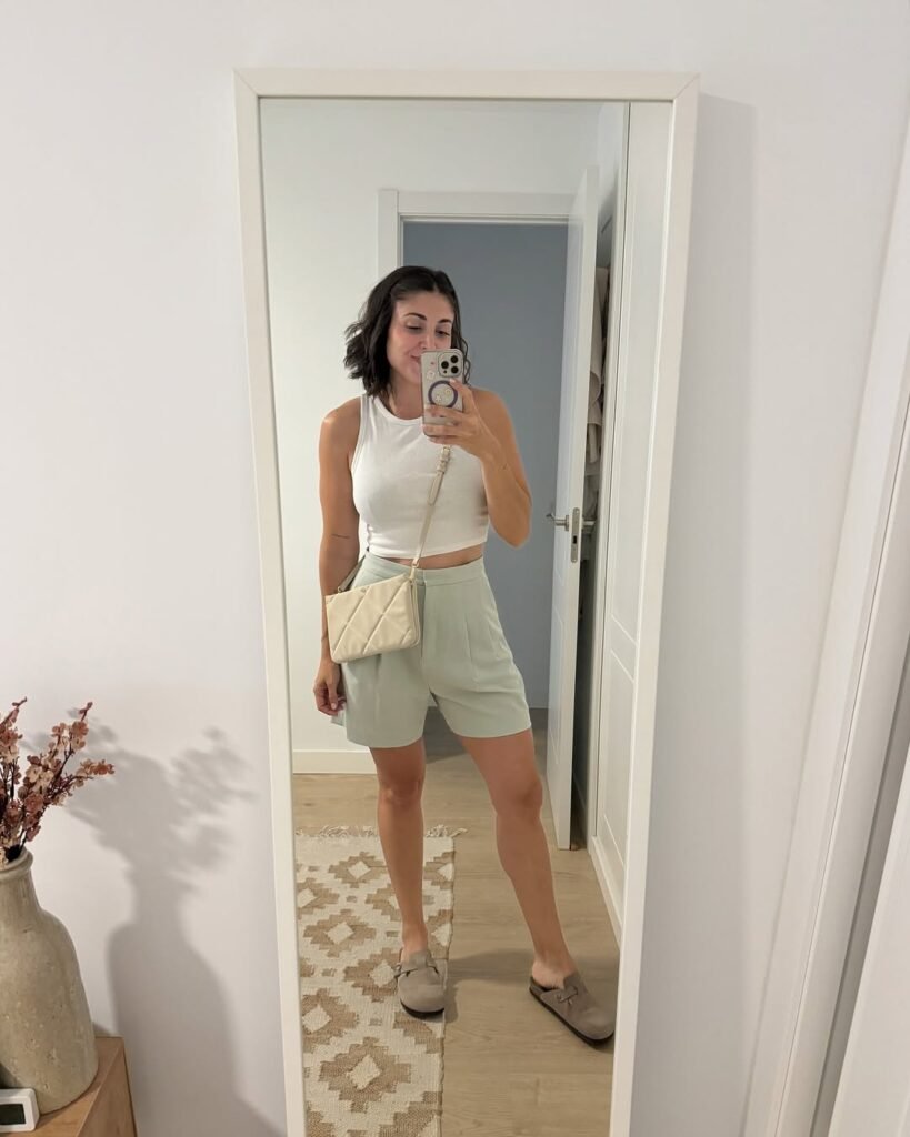 Alba García Diez posando frente al espejo con pantalones cortos, camiseta y bolso, mostrando su estilo casual y relajado.