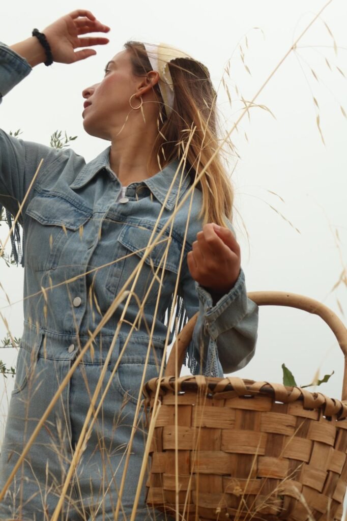 Alicia García mirando hacia arriba mientras sostiene una canasta y lleva un conjunto de mezclilla con diadema.