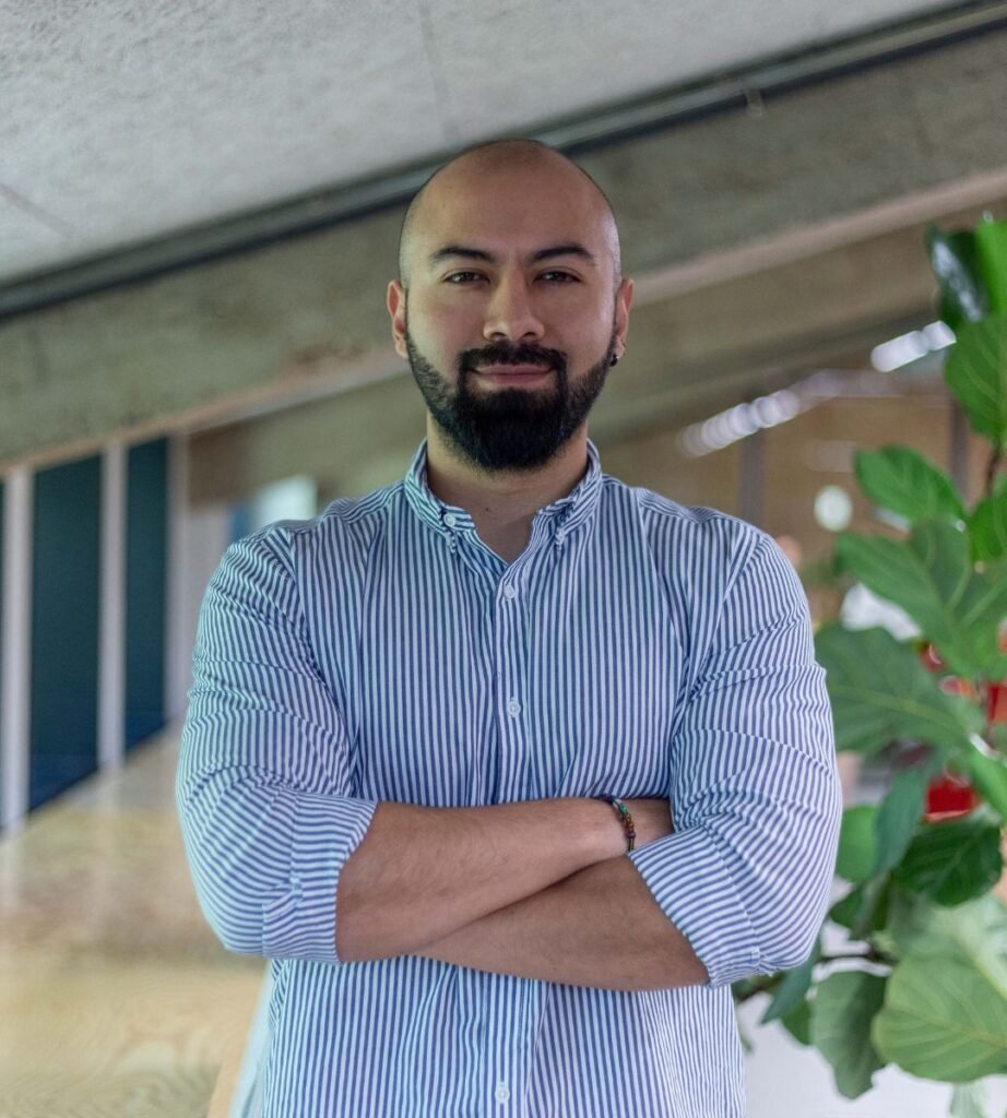 Juan Sebastián Cruz posando con los brazos cruzados, usando una camisa a rayas, con fondo de planta y ambiente moderno.