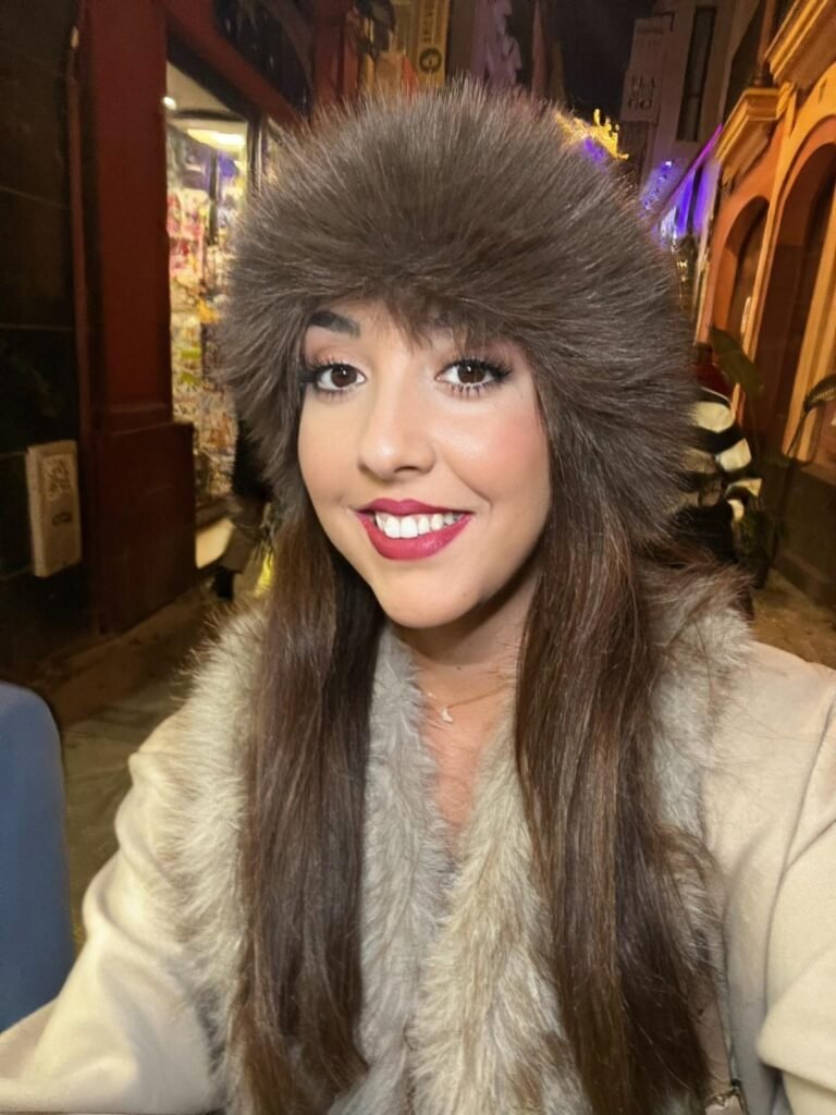 Lola Martín González usando un gorro de peluche en una noche iluminada con luces cálidas.