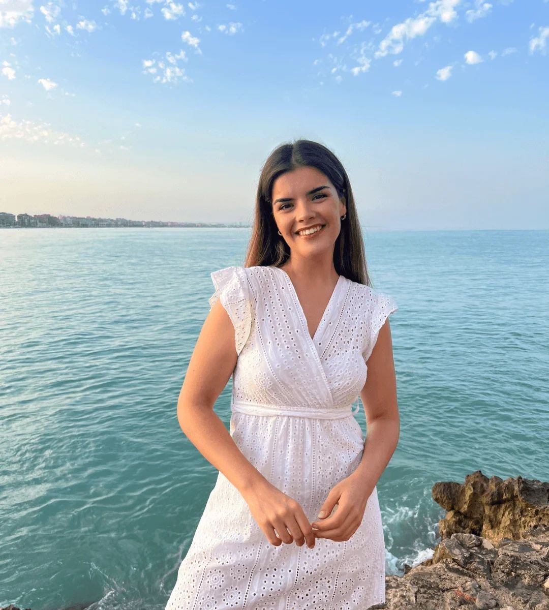 Sara Herrero, influencer UGC de moda, posando con un vestido blanco frente al mar y el cielo despejado.