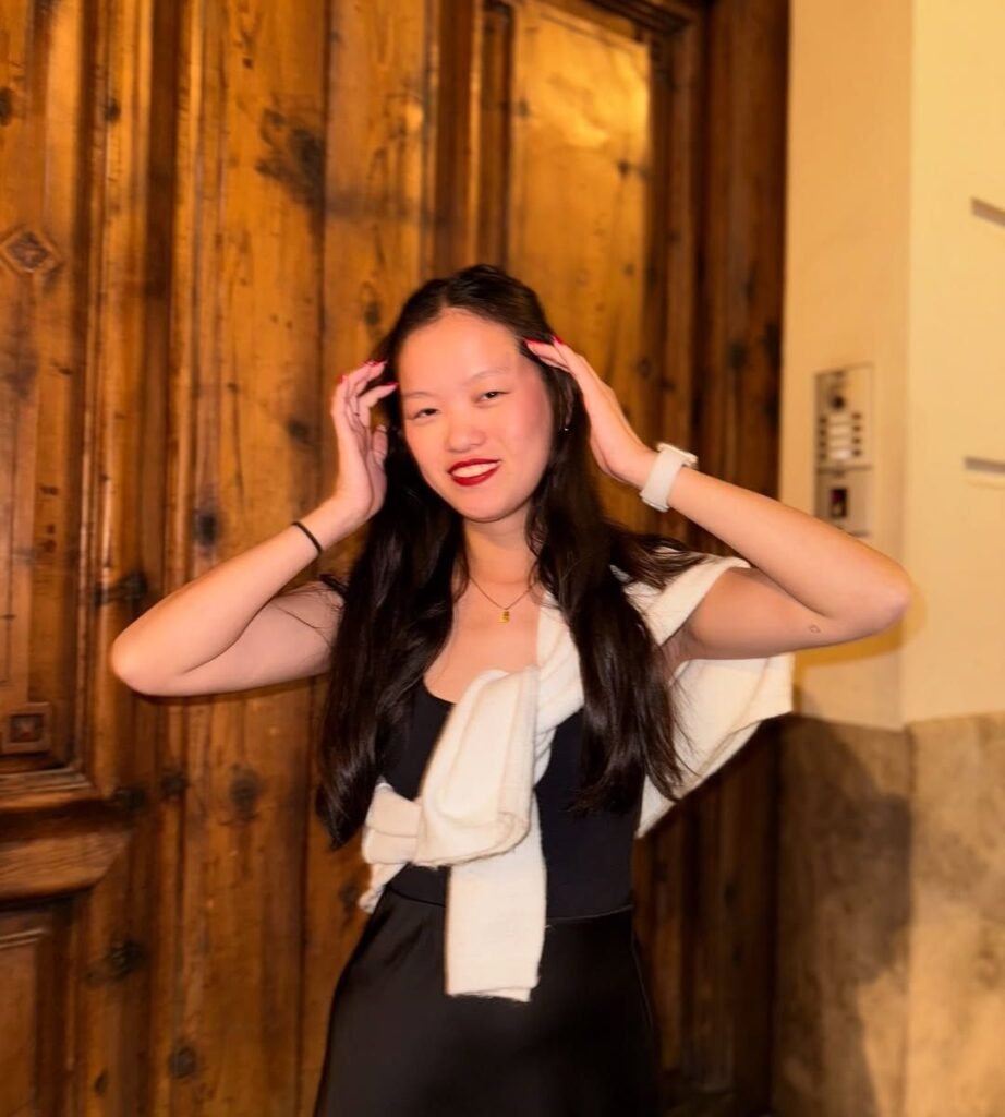 Agencia de marketing digital Brilla Influencers y Comunicación, María Bedins con vestido negro y suéter blanco, posando con las manos en el cabello frente a fondo de madera.