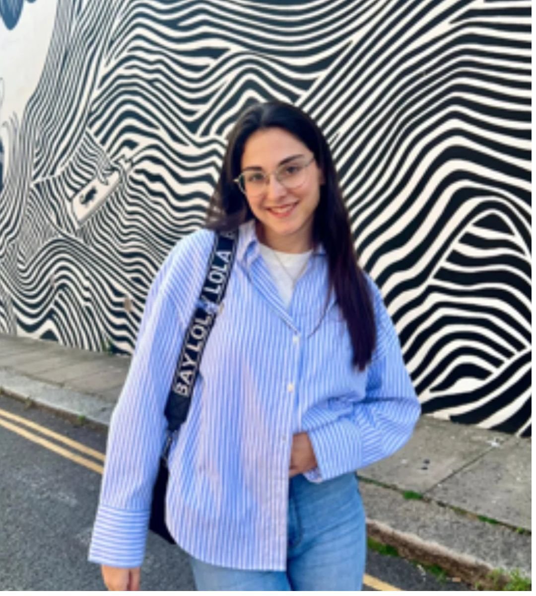 Marta de Gracia posando con camisa de rayas frente a mural artístico, en colaboración con la Agencia de Marketing Digital Brilla Influencers y Comunicación.