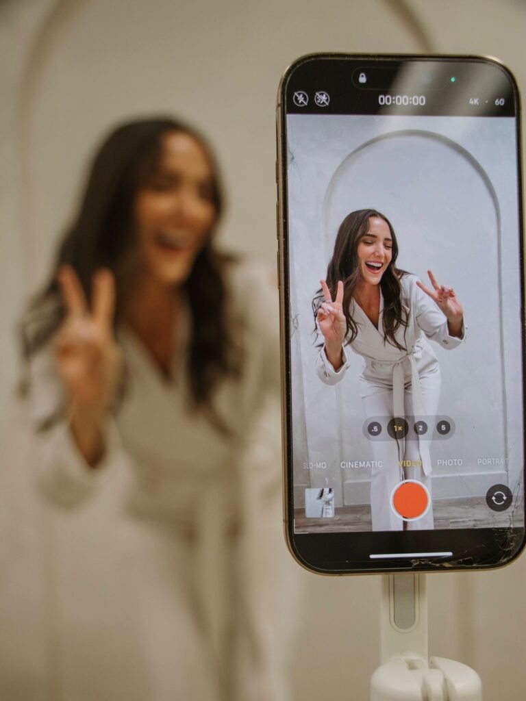 Mujer influencer tomando un selfie con teléfono móvil mientras posa en un estudio con fondo neutro.