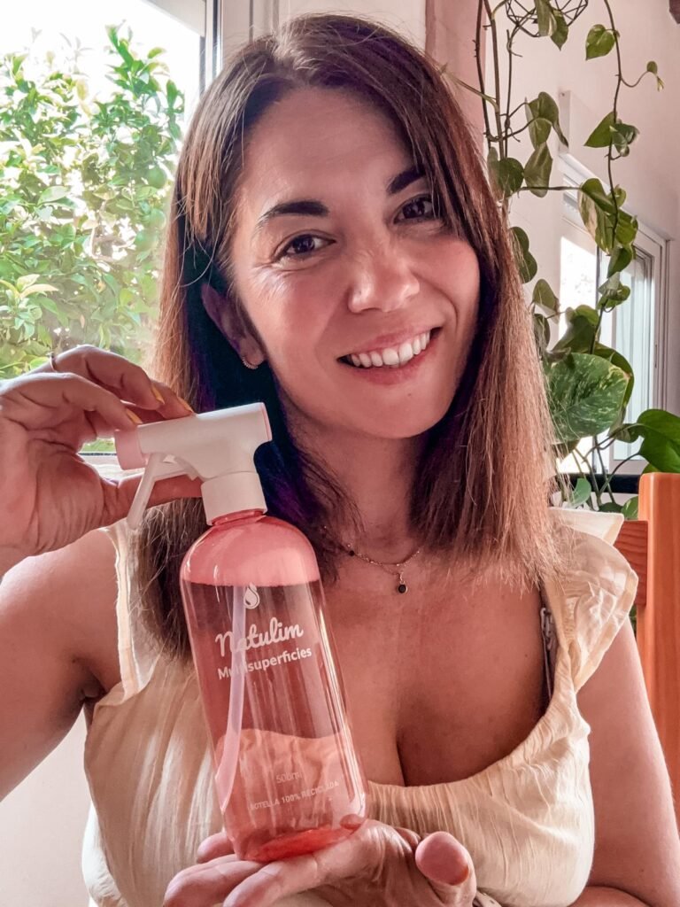 Laura Tur sosteniendo una botella de limpiador multiusos Natulim, con un fondo de plantas en su casa