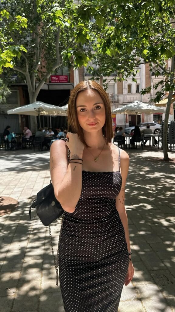 Mujer con vestido negro en terraza urbana con luz natural y ambiente relajado.