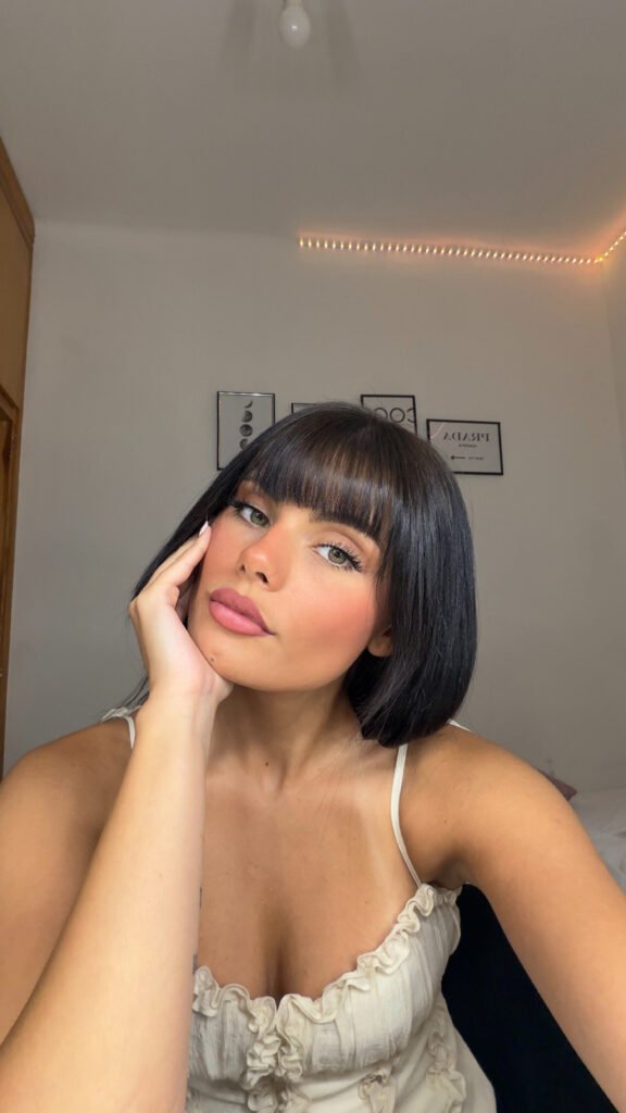 Nerea Torres posando en una habitación de estilo minimalista con iluminación cálida, cabello negro corto con flequillo y top blanco con volantes.