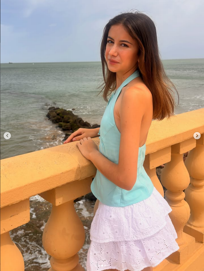 Chica joven posando junto al mar con outfit veraniego azul y blanco
