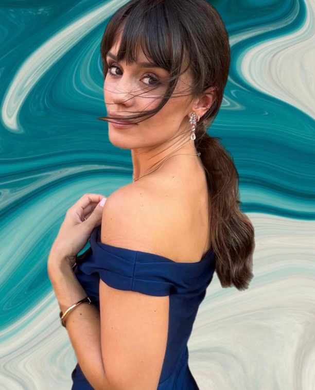 Esther Arribas Checa con vestido azul marino, peinado recogido y pendientes brillantes en retrato elegante sobre fondo artístico verde.