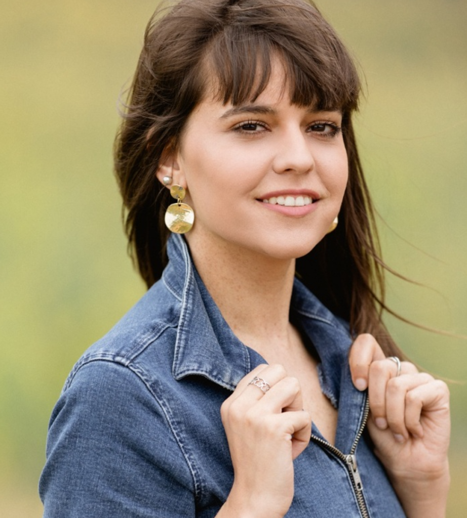 Paula sonriendo con chaqueta vaquera y pendientes dorados en una sesión lifestyle al aire libre
