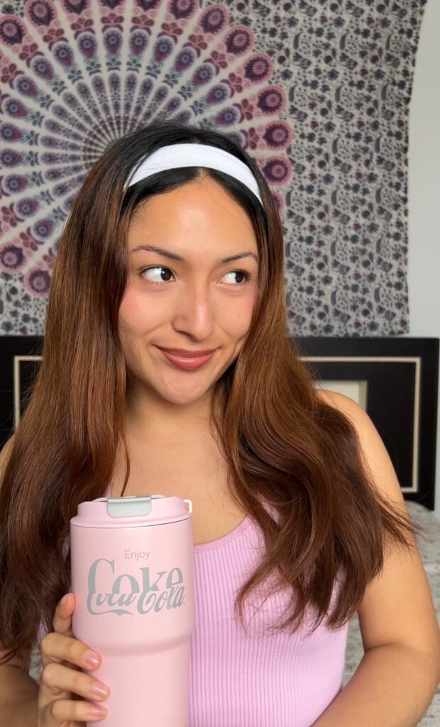 Noelia García sosteniendo un vaso de Coca-Cola rosa, sonriendo y mirando hacia un lado