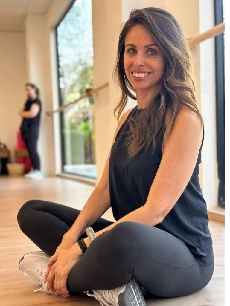 Mujer sonriendo en ropa deportiva, sentada en el suelo de una sala de ejercicio.