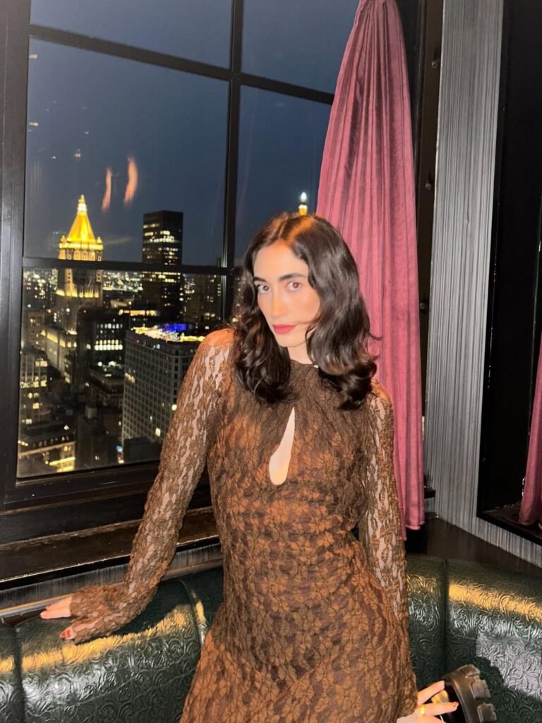 Ana Flores Campos posando en un elegante espacio urbano nocturno con vistas panorámicas a la ciudad, luciendo un vestido de encaje marrón de estilo sofisticado y moderno.