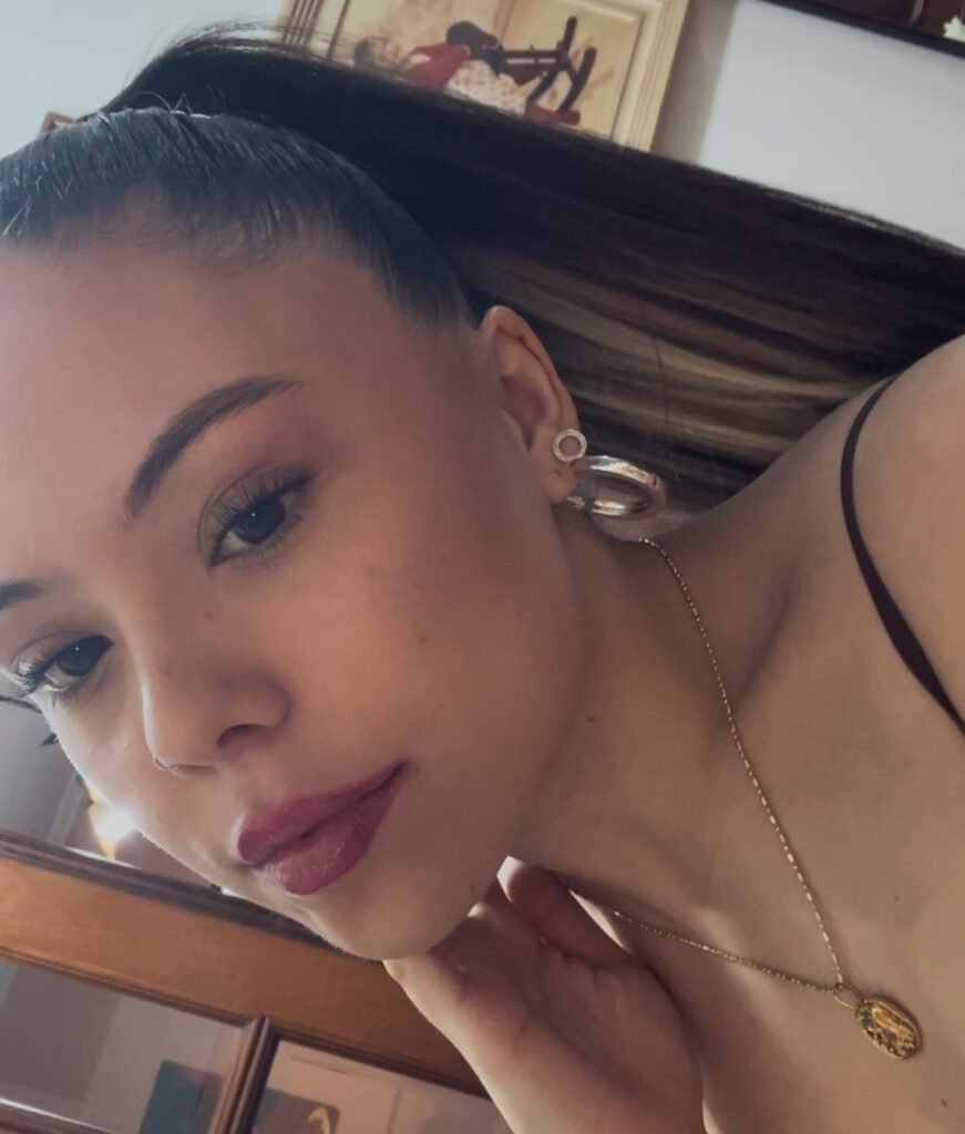 Primer plano de joven con maquillaje natural, peinado recogido y accesorios, en interior elegante.