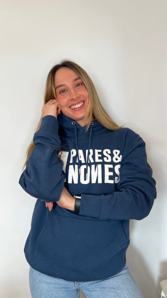 Inés Vidal sonriendo frente a un fondo blanco, vistiendo una sudadera azul marino en una fotografía lifestyle de estilo casual y natural.