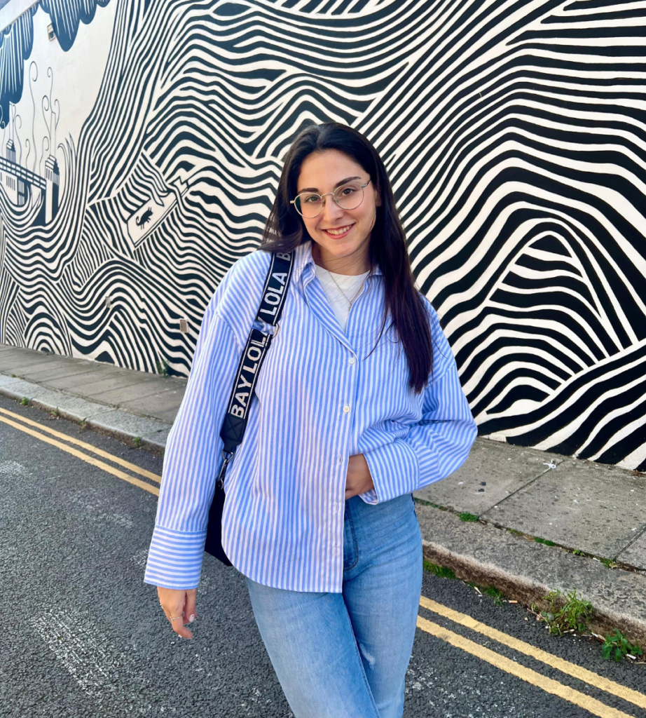 Marta de Gracia posando con camisa de rayas frente a mural artístico, en colaboración con la Agencia de Marketing Digital Brilla Influencers y Comunicación.
