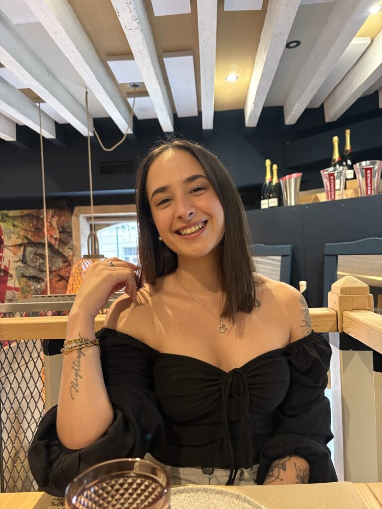 Aitana Nicolao, creadora de contenido de lifestyle y beauty, sonriente en un restaurante con maquillaje natural y look casual.