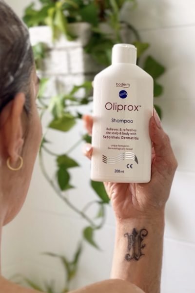Botella de shampoo Oliprox para dermatitis seborreica en mano de mujer