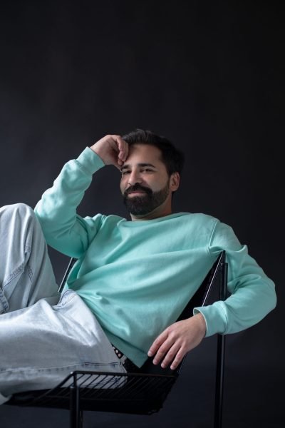 Juan José Marco posando relajado en silla con sudadera verde agua y fondo oscuro
