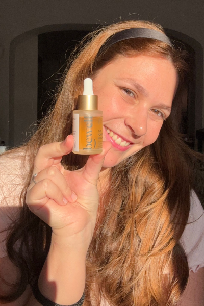 Casandra Benassar sonriente sosteniendo un serum facial, luz natural sobre su rostro, expresión alegre y cercana.