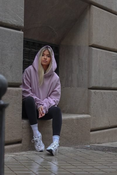Alba Rodríguez posando con sudadera morada y zapatillas en una calle de la ciudad, destacando su estilo único y su colaboración con Brilla Influencers y Comunicación.