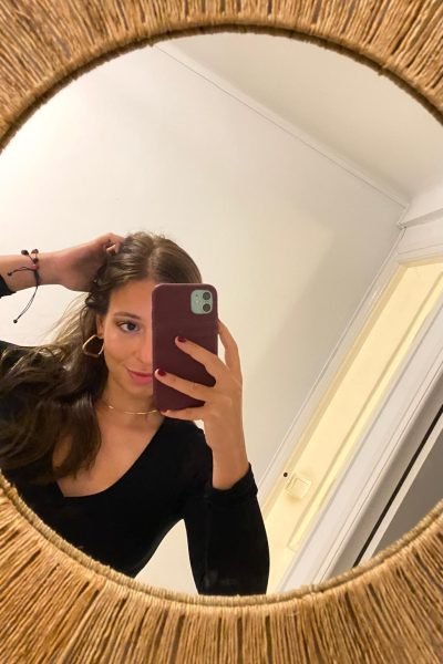 Alicia García posando en una selfie frente al espejo, con una camiseta negra, pendientes dorados y collar.