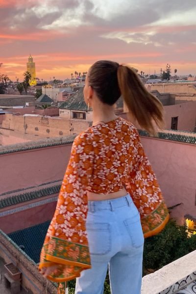 Alicia García mirando un hermoso atardecer en Marruecos, con una blusa roja y jeans.