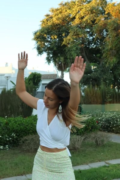 Alicia García bailando en un parque, con un top blanco y falda larga verde claro.