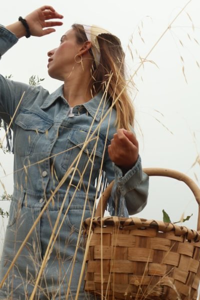 Alicia García mirando hacia arriba mientras sostiene una canasta y lleva un conjunto de mezclilla con diadema.