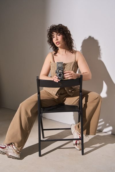 Ana Carpio sentada en una silla sujetando una cámara fotográfica analógica durante una sesión de estudio. Una imagen que representa creatividad, fotografía y producción de contenido.