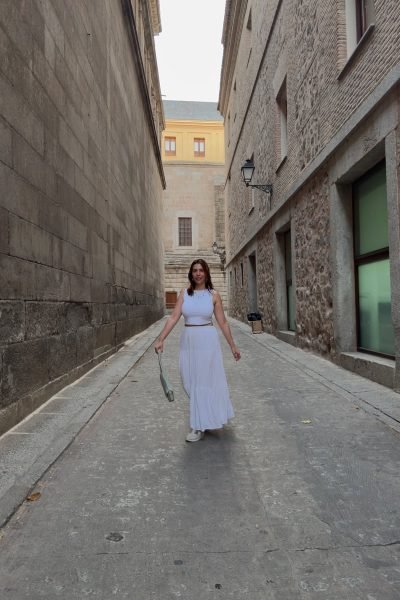 Ana Carpio paseando por una calle histórica con un conjunto blanco y un bolso de mano. La imagen transmite elegancia, naturalidad y un estilo lifestyle ideal para campañas de turismo, moda y contenido UGC.