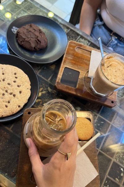 Ana Carpio disfrutando de un café helado acompañado de galletas artesanales en una cafetería. Una escena lifestyle que transmite cercanía, ocio y momentos cotidianos.
