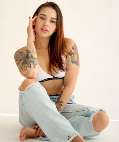 Bárbara Elena sentada en el suelo, con jeans rotos y camiseta blanca, mostrando una actitud relajada y natural.
