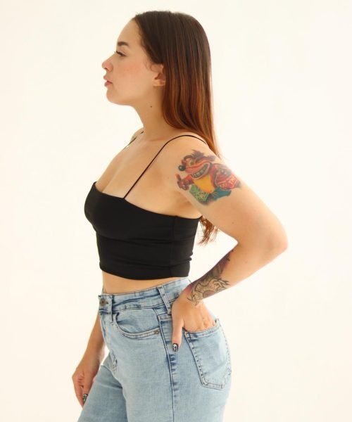 Bárbara Elena de perfil, con top negro y jeans, mostrando sus tatuajes y una postura confiada.