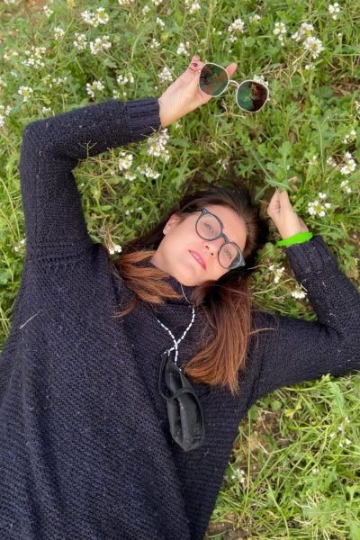 Carolina Marzá tumbada sobre la hierba rodeada de flores silvestres en un entorno natural.