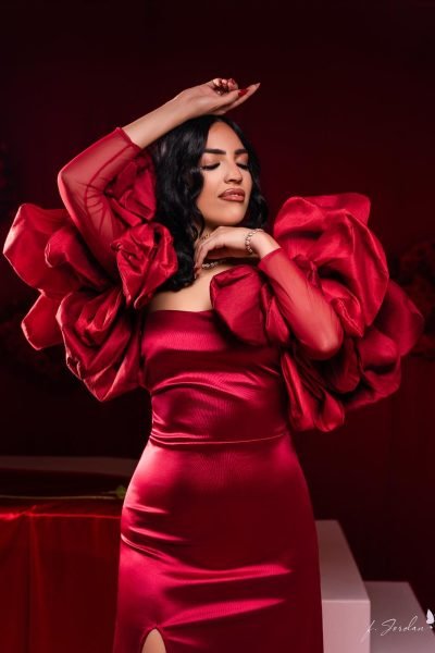 Carolina Vera posando en vestido rojo con detalles voluminosos en los hombros, estilo elegante y sofisticado. UGC de moda de alta costura.