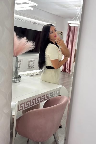Carolina Vera en selfie con vestido blanco, fondo moderno con decoración elegante. UGC casual y chic.