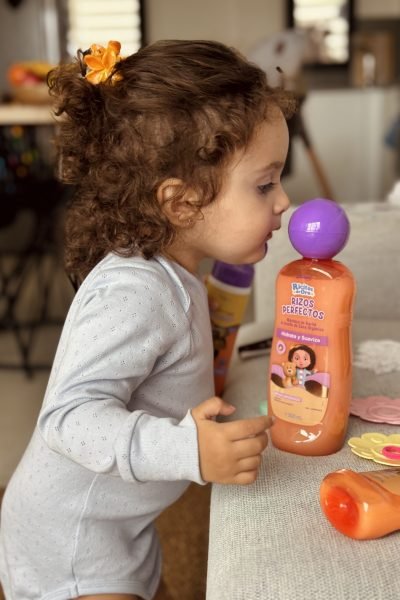 Niña pequeña oliendo el champú rizos perfectos, con su cabello rizado y una actitud curiosa.