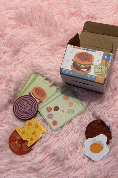 Juguete de hamburguesa A Bite of Hamburger con piezas de comida y cartas, en fondo suave.