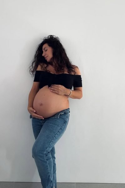 Cinzia Ledonne abrazando su barriga embarazada, sonriendo de manera tranquila con fondo blanco.