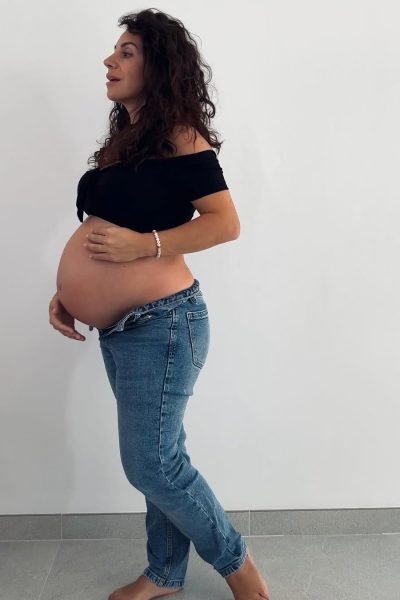 Cinzia Ledonne posando con jeans y camiseta negra durante el embarazo, tocando su barriga.