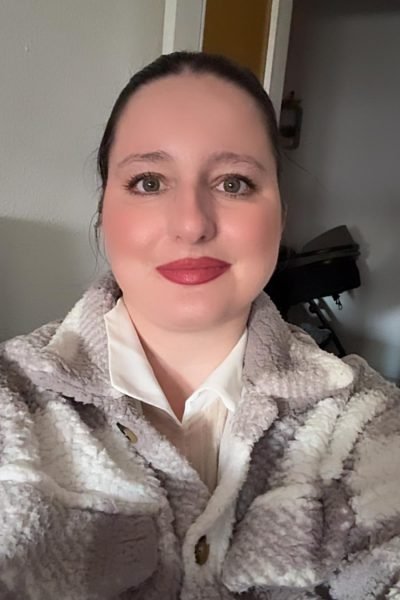 Cristina en su casa con una camiseta gris y chaqueta de lana, mirando a la cámara con una sonrisa mientras está en un ambiente acogedor. Título: Cristina en su hogar, relajada y sonriente