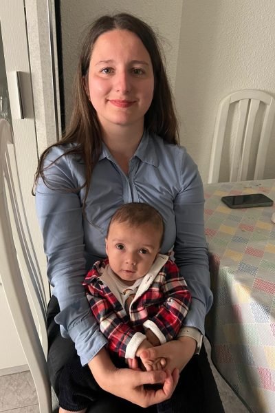 Cristina con su bebé, ambos sonriendo en un ambiente familiar, disfrutando de una comida en la mesa.