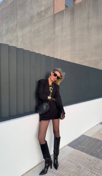 Dessire Verdu Zarco posando con un elegante conjunto negro y botas altas, en un fondo arquitectónico, creando contenido visual de moda para Agencia de marketing digital Brilla Influencers y Comunicación