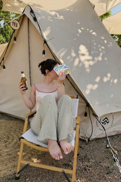 Esther Zecchin disfrutando de una experiencia glamping al aire libre mientras juega a las cartas y sostiene una bebida refrescante.