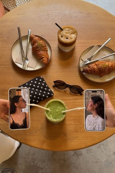 Mesa de cafetería con café, matcha, croissants y teléfonos móviles mostrando una videollamada en un entorno lifestyle.