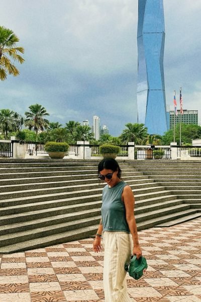 Fátima del Pilar caminando por una plaza moderna con un rascacielos icónico de fondo.